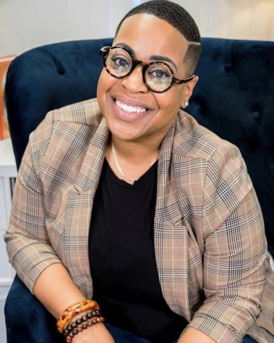 Sheena, owner and stylist of The Sanford Style, smiling in round glasses and a plaid blazer