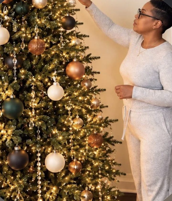 Sheena hanging an ornament on a lit Christmas tree styled in copper, cream and green